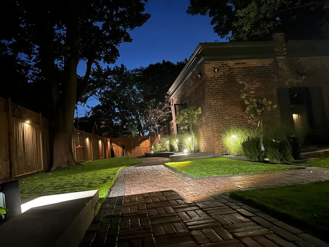backyard walkway with landscape lighting, brick path and illuminated lawn at night