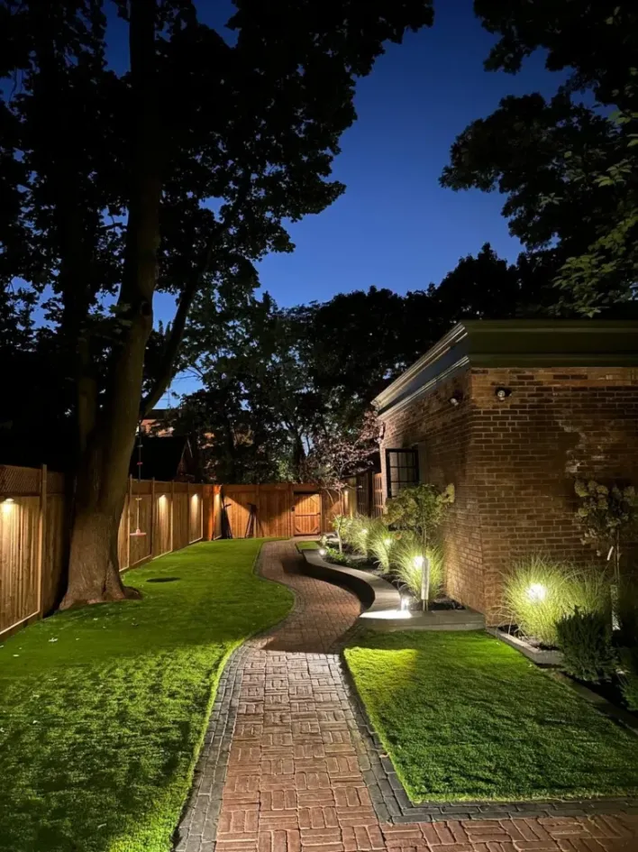 curved brick pathway with landscape lighting, lawn and garden beds illuminated at night
