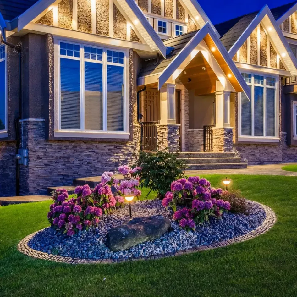 front yard flower bed with landscape lighting, decorative stones and blooming plants near house entrance