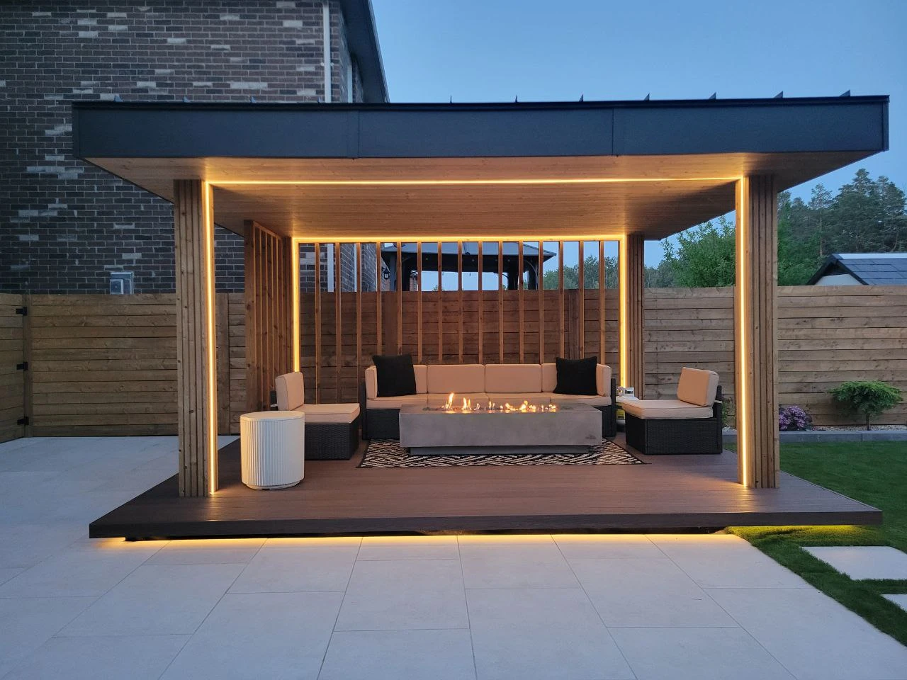 modern backyard pergola with built in fire pit seating area and ambient lighting