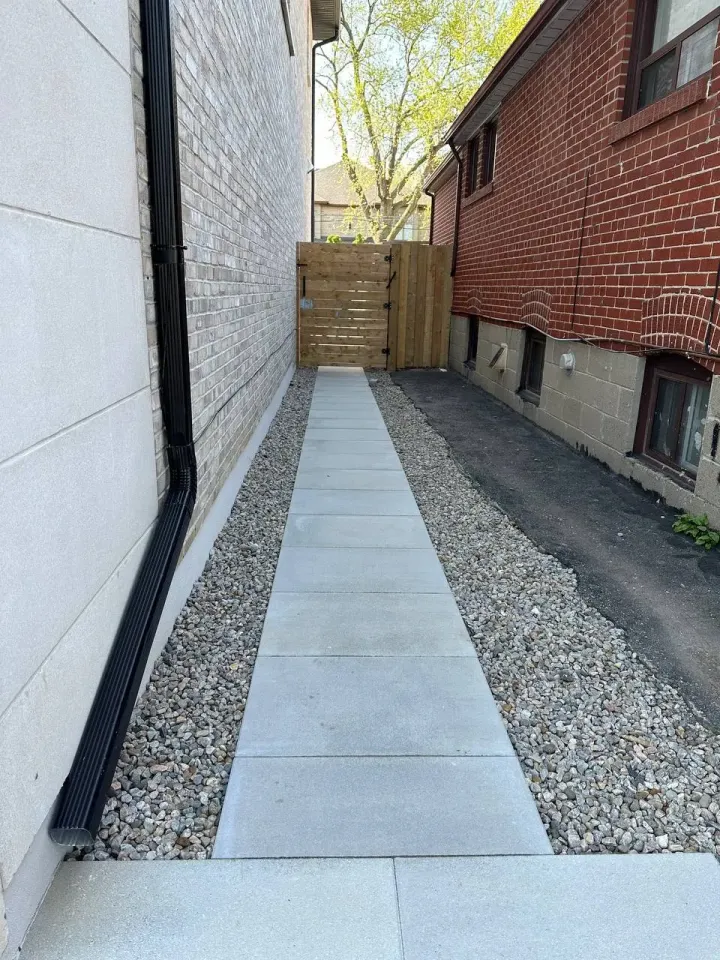 side yard landscaping with concrete walkway gravel and wooden gate between houses