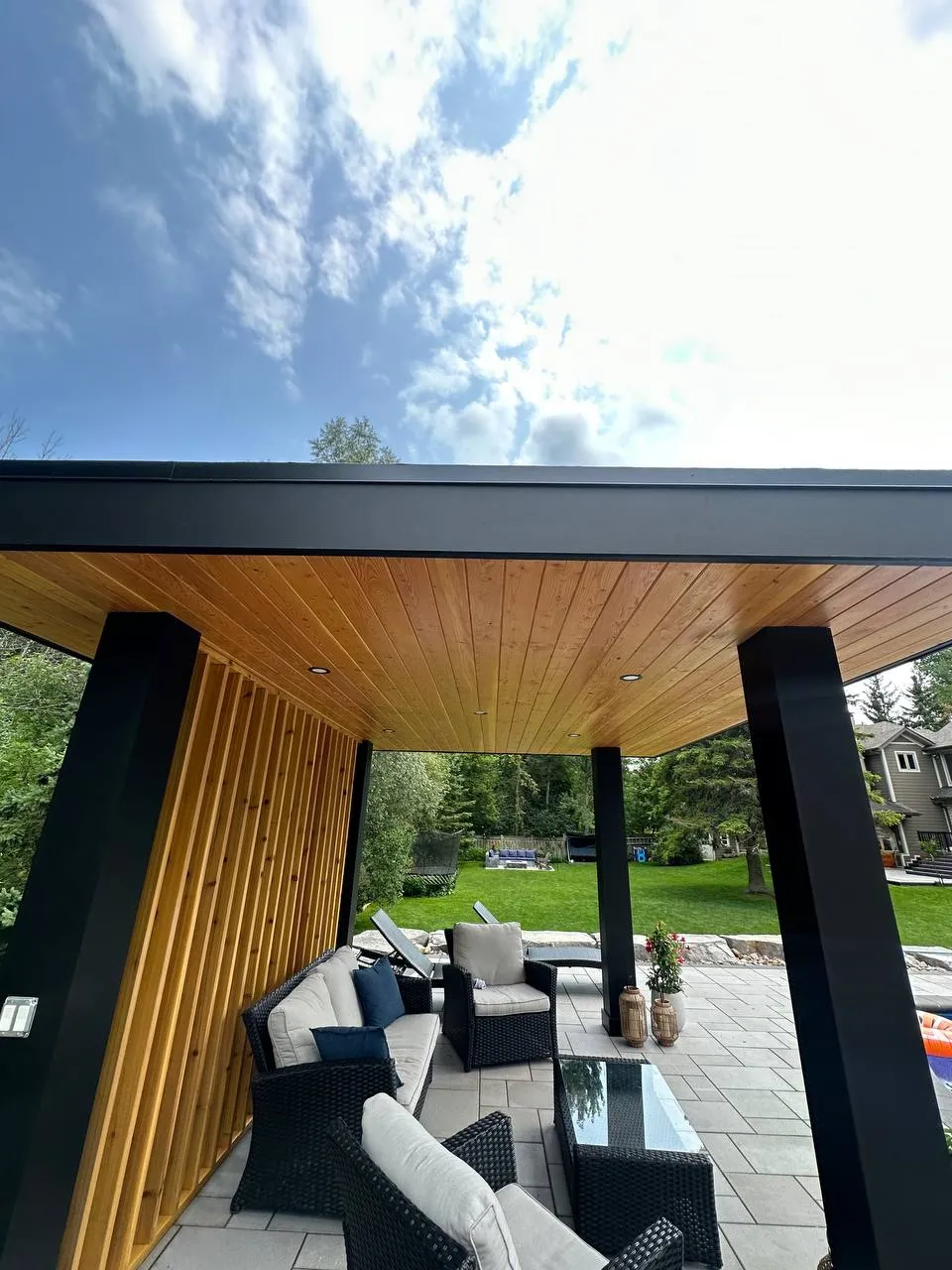 covered backyard patio with black pergola, wood ceiling and outdoor lounge seating