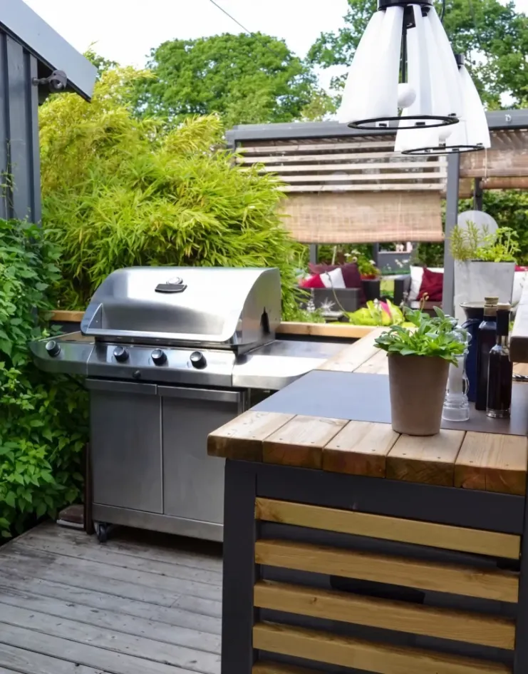 backyard outdoor kitchen with grill, wooden deck, countertop and greenery around