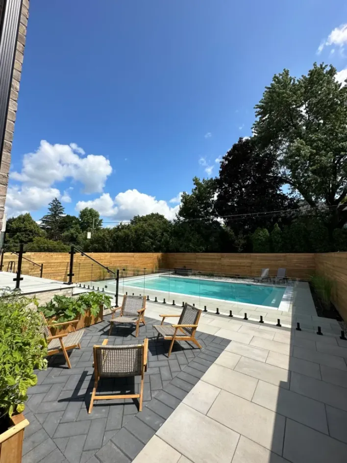 modern backyard with pool, large stone patio, glass fence, outdoor seating area, and wood privacy fencing