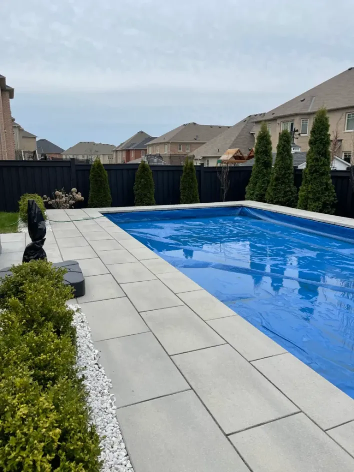 modern backyard pool with large concrete pavers, clean coping edges, black fence, and minimalist landscaping
