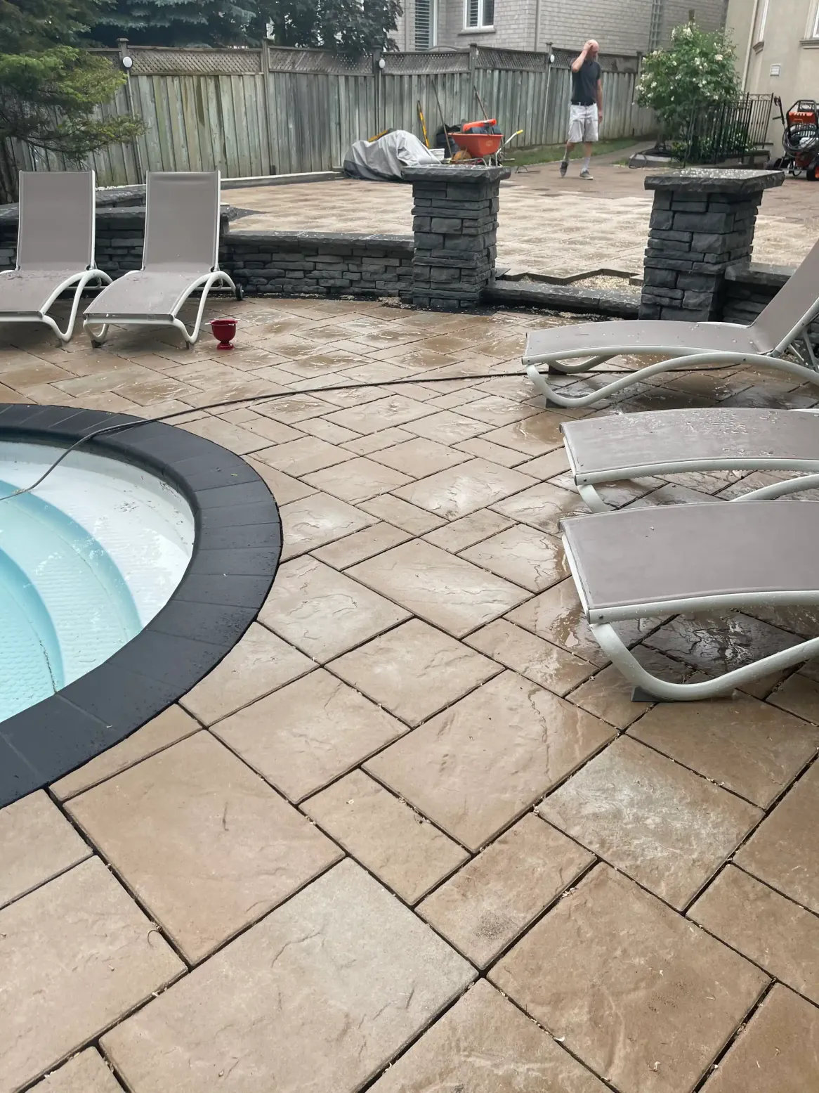 poolside patio with interlocking stone pavers, lounge chairs, and raised stone wall with pillars