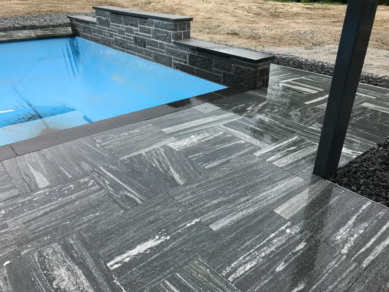 modern poolside with gray marble pavers, raised stone wall, and clean geometric patio design