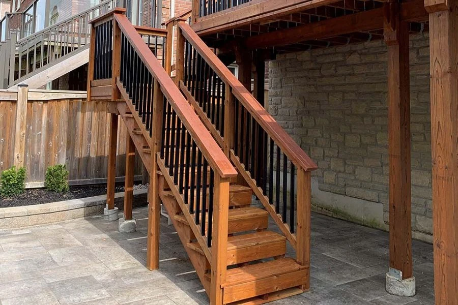 Wood deck stairs with black metal balusters and paved patio below
