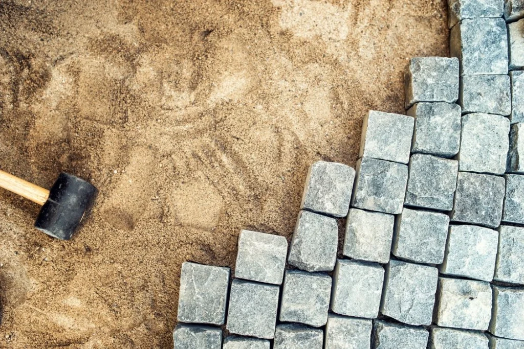 Close-up of interlocking stone pavers being installed on sand base with rubber mallet
