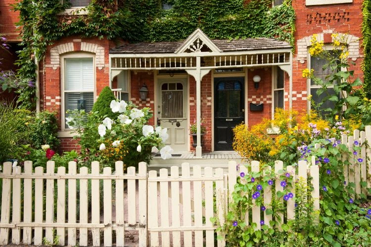 Charming white picket fence with lush front garden and brick home exterior