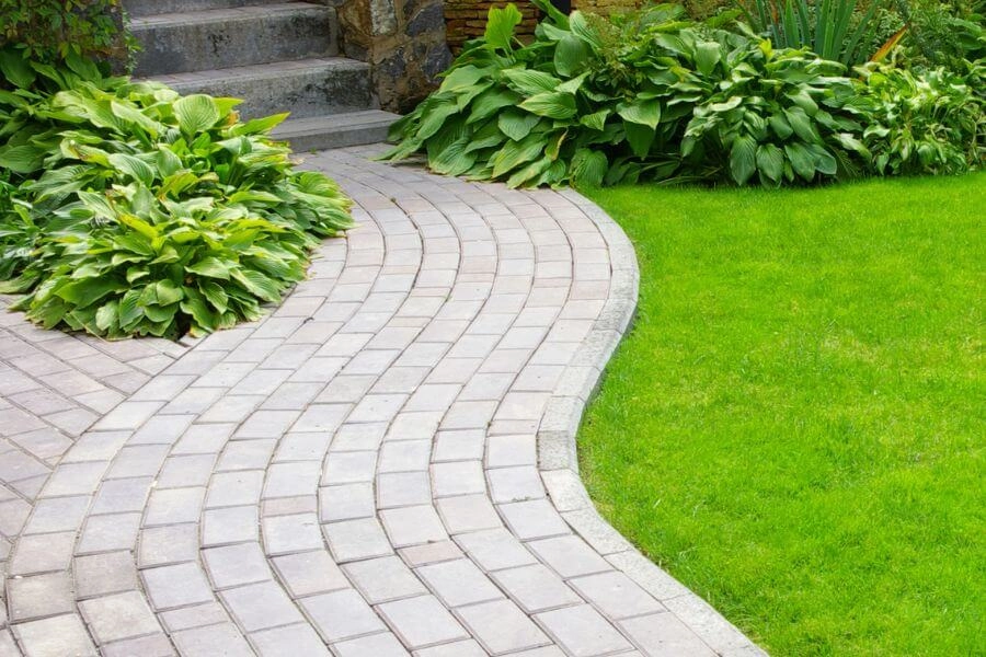 Curved interlocking walkway with garden plants and lawn, image by OAKS Home Services