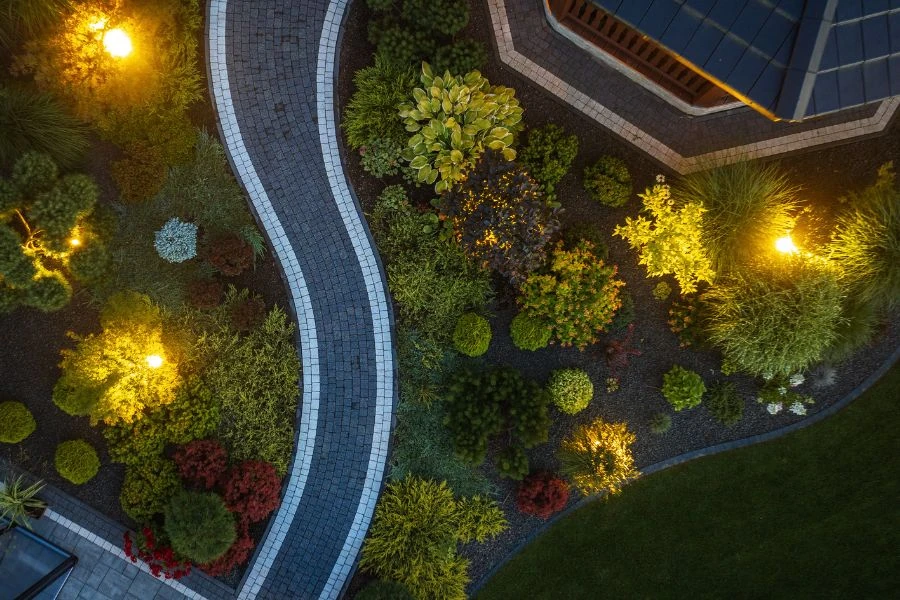 Interlocking walkway with landscape lighting highlighting trees and garden beds, image by OAKS Home Services