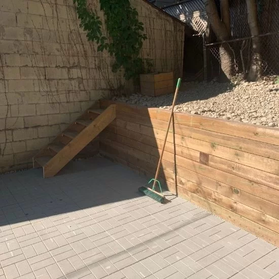 Gray interlocking stone patio with wooden retaining wall and landscaped slope, image by OAKS Home Services