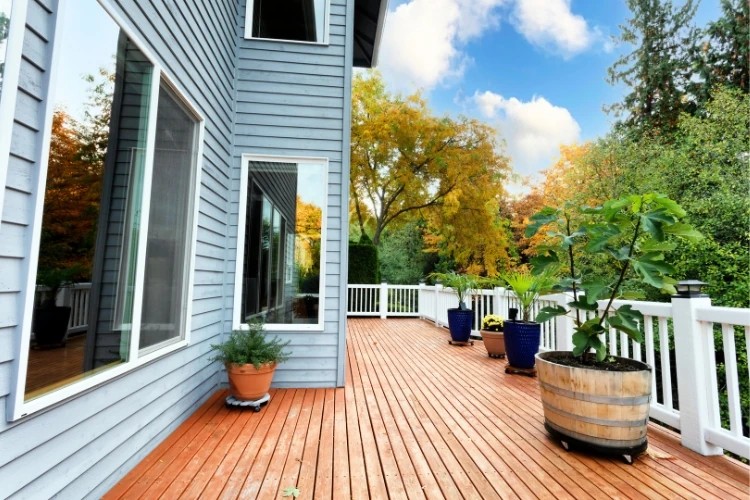 Spacious wooden deck with white railing and potted plants beside modern home