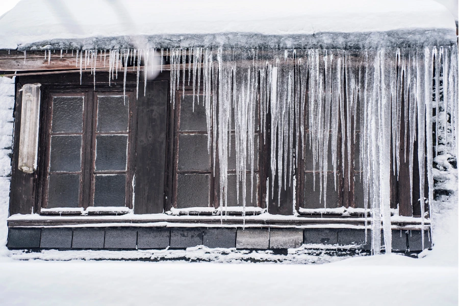 Long icicles hanging from roof edge and frozen windows during severe winter freeze