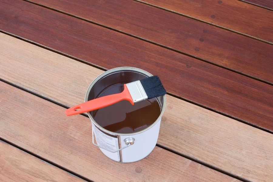 Can of wood stain with brush on freshly stained deck boards