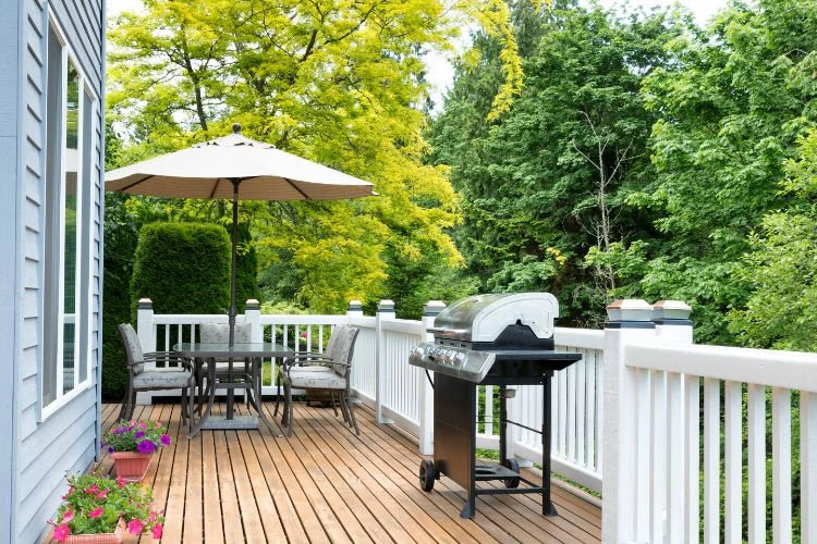 Backyard wooden deck with white railing, outdoor dining set, and barbecue grill setup