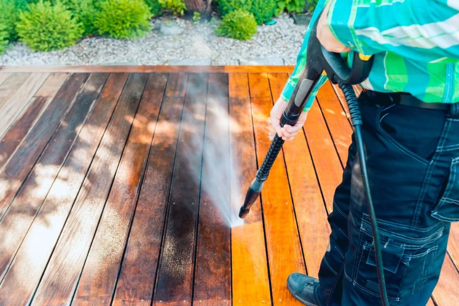 Person power washing wooden deck boards to restore and clean surface