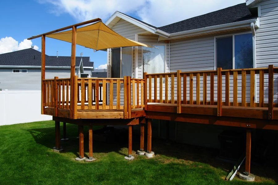 Elevated wood deck with railing and shade canopy over backyard lawn